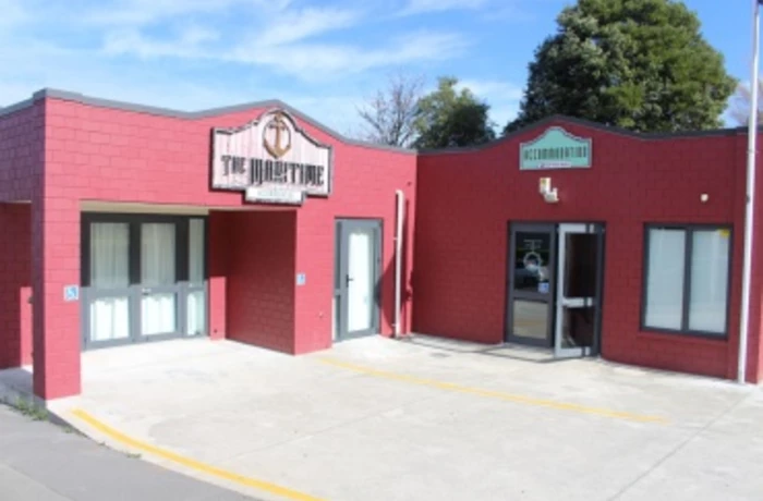 the front entrance of The Maritime painted red l shaped building with several windows and signage above the door.